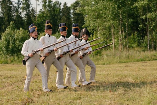 Soldiers in historical uniforms marching during a reenactment in nature.