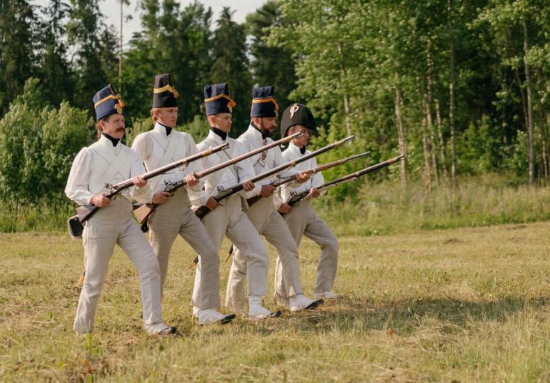 Soldiers in historical uniforms marching during a reenactment in nature.